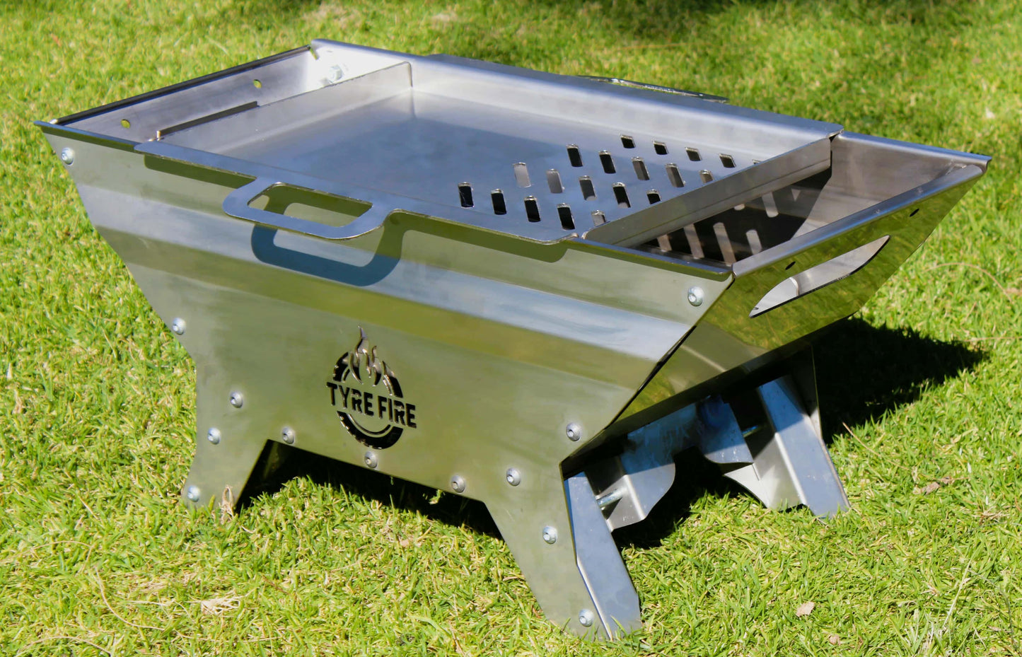 Stainless fire pit on grass with 'Tyre Fire' branding and grill plate