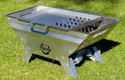 Stainless fire pit on grass with 'Tyre Fire' branding and grill plate